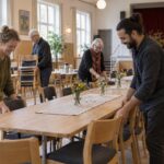 Mennesker samles omkring et bord i et lyst forsamlingslokale